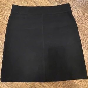 Svart kjol med dragkedja - Snygg svart kortkjol med dragkedja bak. Perfekt för en stilren look. Kjolen har en enkel design som gör den lätt att matcha med olika toppar.