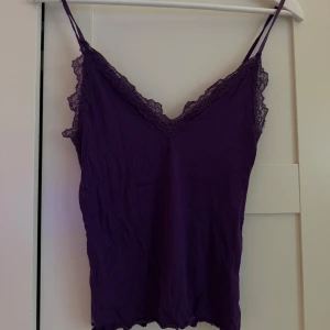 Lila ribbad linnetopp med spetsdetaljer - Snygg lila linnetopp med ribbad struktur och spetsdetaljer längs v-ringningen. Den är från new Yorker och är i storlek S