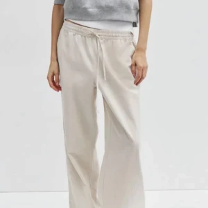 Beige linnebyxor från H&M - Säljer ett par bekväma och stilrena beige linnebyxor från H&M. De har en elastisk midja med snörning för extra komfort. Perfekta för en avslappnad sommarlook!