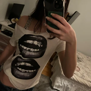 Vit offshoulder t-shirt - Säljer en cool vit offshoulder t-shirt med ett stort tryck av svarta läppar. Perfekt för en avslappnad stil med en twist. T-shirten har en lös passform och är superbekväm att bära.