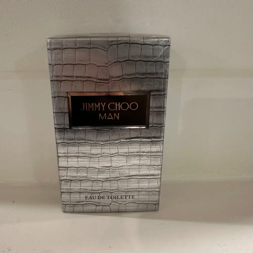Säljer en elegant Jimmy Choo Man Eau de Toilette i en stilren förpackning med krokodilskinnsmönster. Flaskan innehåller 50 ml av denna maskulina doft, perfekt för den moderna mannen. Tillverkad i Frankrike.. Perfume.