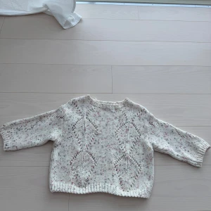 Vit stickad tröja med mönster - Säljer en mysig vit stickad tröja med ett fint hålmönster. Tröjan har trekvartsärmar och en avslappnad passform, perfekt för kyligare dagar. Den är både stilren och bekväm.