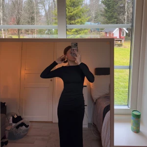 Svart långklänning med slits - Snygg svart långklänning med en elegant slits på sidan. Klänningen har en tight passform och långa ärmar, perfekt för en stilren look. Den är ribbad i tyget, men mjuk som formar sig fint efter kroppen. Använd 1 gång 