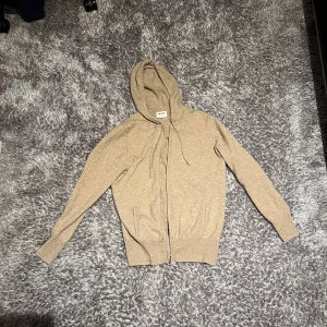 Soft Goat zip huvtröja - Säljer en stilren beige hoodie från Soft Goat. Den har en dragkedja framtill och en praktisk huva med snören. Perfekt för en avslappnad look. Passar bra till både jeans och mjukisbyxor. Nypris: ca 2500kr