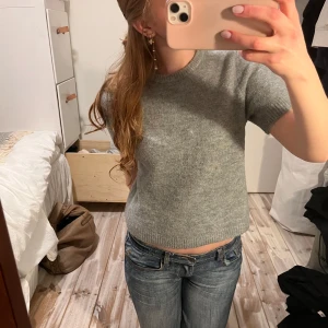 Grå stickad tröja - Säljer en stilren grå stickad tröja med korta ärmar. Tröjan passar perfekt för en avslappnad look. Perfekt för både vår och höst. 