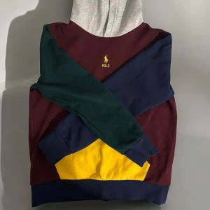 Flerfärgad hoodie från Polo Ralph Lauren - Säljer en äkta cool flerfärgad hoodie från Polo Ralph Lauren. Tröjan har en mix av vinröd, grön, blå och gul färg med en grå huva. Den har en stor ficka framtill och det klassiska Polo-logotypen broderad på bröstet. Passar folk mellan 160-170 cm. Tröjan är i nytt skick inga defekter eller något men använd 1-3 gånger. Perfekt för en avslappnad stil! 