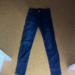 Mörkblå jeans från Lee - Snygga mörkblå jeans från Lee med en klassisk femficksdesign. De har en knappgylf och är perfekta för en stilren look. Passformen är smal och de är tillverkade i ett slitstarkt denimtyg.