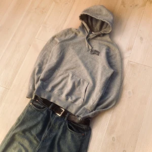 Grå hoodie från Billionaire Boys Club - Säljer en grå hoodie från Billionaire Boys Club med tryck på bröstet och en liten astronautdetalj på ärmen. Tröjan har en klassisk känguruficka och justerbar huva med snören. Perfekt för en avslappnad stil.