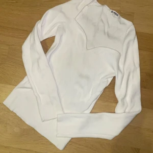 Vit långärmad tröja från Off-White - Säljer en stilren vit långärmad tröja från Off-White. Tröjan har en unik asymmetrisk design vid halsen och är tillverkad i ett mjukt material. Perfekt för en trendig och modern look.