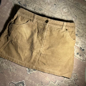 Beige manchesterkjol från Vero Moda - Säljer en snygg beige manchesterkjol från Vero Moda. Kjolen har en klassisk design med fickor fram och bak samt en knapp i midjan. Perfekt för en stilren look!