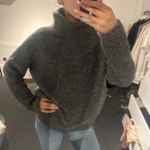 Grå stickad polotröja - Mysig grå stickad polotröja perfekt för kyliga dagar. Tröjan har en hög krage och långa ärmar, vilket ger en varm och bekväm känsla. Passar utmärkt till jeans för en avslappnad look.