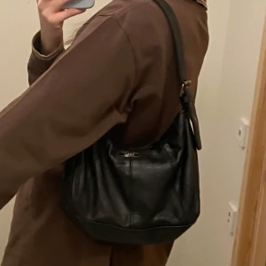 Svart axelväska i skinn - Snygg svart axelväska i skinn med justerbar axelrem och dragkedja! Fint skick