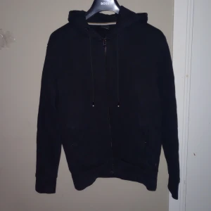 Svart hoodie från Hugo Boss - Säljer en stilren svart hoodie från Hugo Boss. Den har en dragkedja framtill och justerbar huva med snören. Säljer tröjan pga att den är för liten sant att jag tröttnat på den. Den är storlek M och passar de mästa. Rimliga byten kan accepteras 
