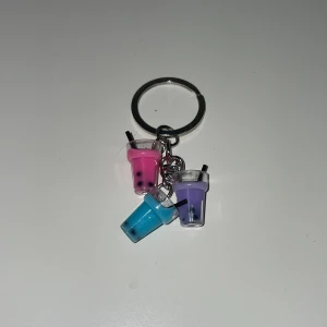 Nyckelring med bubble tea-design - Charmig nyckelring med tre små bubbelte-koppar i rosa, blå och lila. Varje kopp har ett sugrör och små svarta pärlor som liknar tapiokapärlor. Perfekt accessoar för bubbelte-älskare! Kan hängas på vad som helst, exempelvis som nycklar och väska