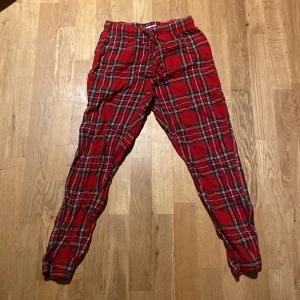 Röda rutiga byxor med snörning - Snygga röda byxor med rutig design och snörning i midjan. Perfekta för en avslappnad stil med en touch av färg. De har en bekväm passform och är lätta att matcha med olika toppar.