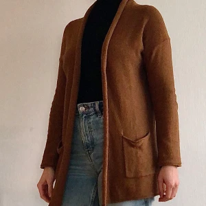 Brun cardigan från H&M - Säljer en mysig brun cardigan från H&M Basic. Den har en öppen design utan knappar och två praktiska fickor framtill. Perfekt för lager-på-lager under kyliga dagar. Fint skick. Nyfixad med nopp-borttagare.  (Finns på fler säljsidor)