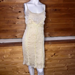 Beige klänning med spetsdetaljer - Charmig beige klänning med vackra spetsdetaljer och broderier. Den har smala axelband och en lätt transparent look med ett romantiskt mönster. Perfekt för en somrig dag eller en speciell kväll.