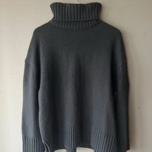 Grå polotröja - Säljer en stilren grå polotröja med ribbade detaljer vid krage, ärmslut och nederkant. Perfekt för kyliga dagar med sin mjuka och bekväma passform. Tillverkad i en blandning av ull och polyester för extra värme och hållbarhet.