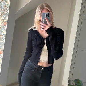 Svart kofta - Snygg svart kofta med v-ringning och knappar framtill. Perfekt för lager-på-lager eller som ett stilrent plagg i garderoben. Den har långa ärmar och en croppad passform.