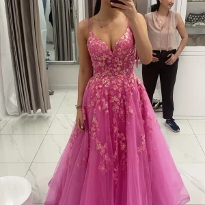 Rosa balklänning med spetsdetaljer - Fantastisk rosa balklänning med vacker spets och blommiga detaljer. Klänningen har smala axelband och en v-ringad urringning som ger en elegant look. Perfekt för speciella tillfällen där du vill känna dig extra glamorös. Den är den sjukaste prinsessklänningen någonsin, har aldeig känne mig så snygg! Köptes för 8600kr