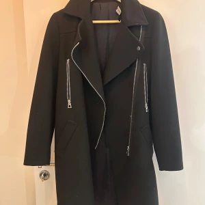 Svart kappa från Zara Woman - Elegant svart kappa från Zara Woman med långa ärmar och stilrena dragkedjedetaljer. Perfekt för kyligare dagar med sin klassiska design och bekväma passform. Tillverkad i ett material som ger en lyxig känsla.