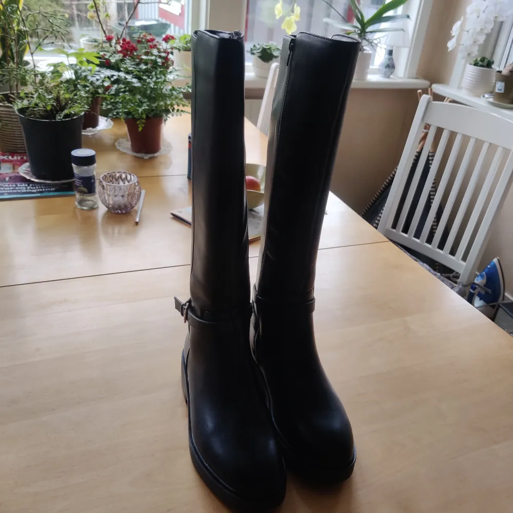Helt nya oanvända svarta knähöga stövlar med ett dekorativt spänne vid ankeln. De har en dragkedja på insidan för enkel på- och avtagning. Storlek 39 från Boohoo. . Kengät.
