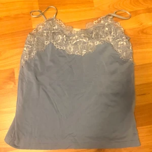 Blå linnetopp med spetsdetaljer från ICHI - Säljer en blå linnetopp från ICHI med vackra spetsdetaljer vid halsringningen. Toppen har tunna axelband. Storlek xs.