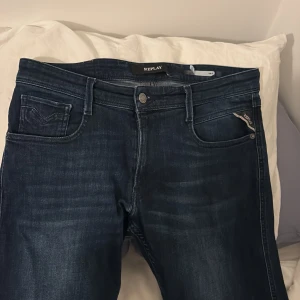 Mörkblå jeans från Replay - Snygga mörkblå jeans från Replay med klassisk femficksdesign. De har en knappgylf och en diskret logga på bakfickan. Perfekta för en stilren look. Storleken är 31-32 slimfit