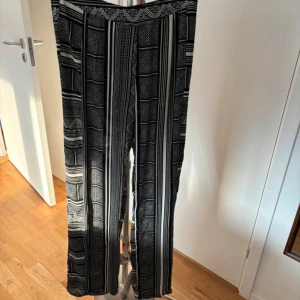 Svartvita mönstrade byxor - Snygga svartvita byxor med ett unikt geometriskt mönster. Byxorna har en rak passform och är perfekta för en stilren look. De är tillverkade i ett mjukt och bekvämt material som ger en skön känsla hela dagen.