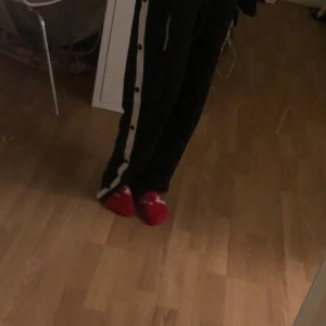 Svarta byxor med vita knappar - Snygga svarta byxor med en vit rand och knappar längs sidorna. Perfekta för en avslappnad stil med en touch av sportig känsla.