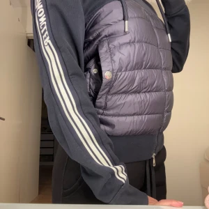 Mörkblå pufferjacka från Moncler  - Snygg svart pufferjacka från Moncler med dragkedja och randiga detaljer på ärmarna. Jackan har en sportig look med en quiltad design och huva med snörning. Perfekt för våren eller höst. Det är unisex så passar både till män och kvinnor . Priset är satt eftersom jackan har en historia bakom skriv gärna privat ifall ni undrar. Den är såklart äkta och scan funkar . 