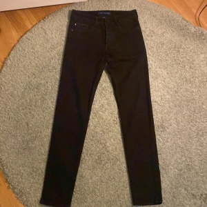 Svarta byxor från HR - Snygga svarta byxor från HR med en klassisk design. De har en rak passform och är perfekta för en stilren look. Byxorna har knappar och en liten fickdetalj framtill.