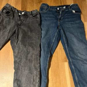 Två par jeans i olika färger - Säljer två par jeans, ett par i svart och ett i klassisk blå denim. Båda har en straight passform med dragkedja och knapp. Perfekta för en avslappnad stil.
