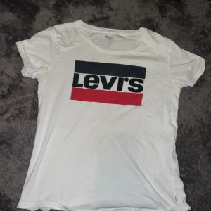 Vit t-shirt från Levi's - Säljer en klassisk vit t-shirt från Levi's med deras ikoniska logga i svart och rött på bröstet. Perfekt för en avslappnad stil. T-shirten är kortärmad och gjord i mjuk bomull.