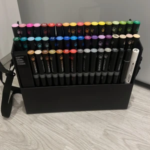 markers från Chameleon - Säljer ett set med Chameleon markers i en praktisk svart förvaringsväska. Setet innehåller 52 olika färger, perfekt för konstnärer och kreativa projekt. Väskan har en axelrem för enkel transport. Tusspennorna funkar parfekt, bara den vita pennan funkar sådär. Bara en stor skada på lådan. nypris- 1800kr