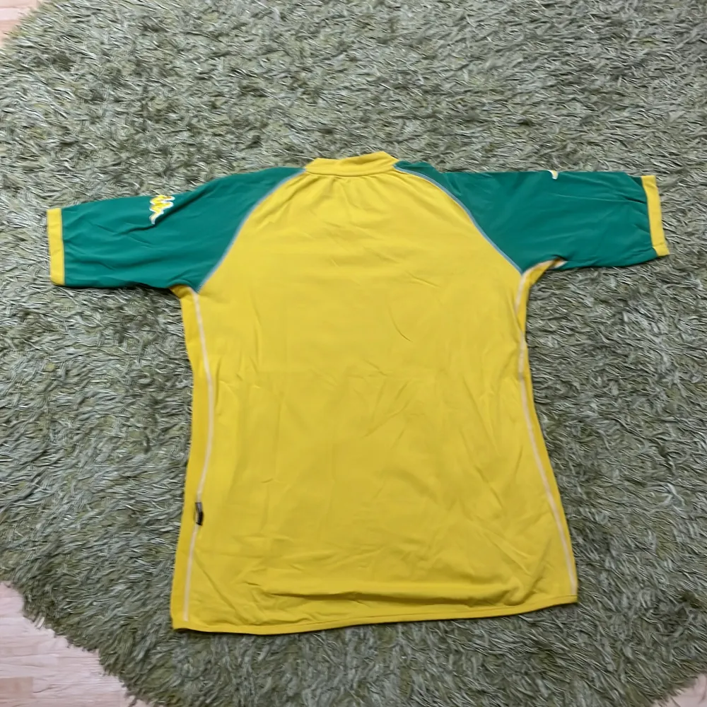Säljer en gul fotbollströja från Kappa med Brasilien-tema. Tröjan har gröna ärmar och ett broderat brasilianskt flaggmärke på bröstet. Stort 'BRAZIL' tryckt på framsidan. Perfekt för fotbollsfans!. T-paidat.