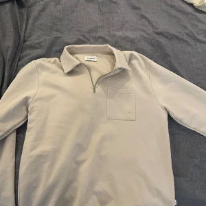 Beige half zip-up från Woodbird - Säljer en stilren beige tröja från Woodbird med dragkedja och krage. Tröjan har en bröstficka och långa ärmar, perfekt för en avslappnad look. Passar bra till det mesta! Hör av dig vid intresse! Nypris ca 550