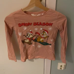 Rosa långärmad tröja från H&M med Disney-motiv - Säljer en söt rosa långärmad tröja från H&M med ett roligt Disney-motiv och texten 'Snow Season'. Perfekt för vintern och julen med sina charmiga detaljer. Tröjan är gjord i mjukt bomullsmaterial.