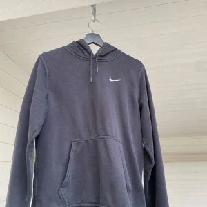 Svart hoodie från Nike - Säljer en klassisk svart hoodie från Nike med den ikoniska loggan på bröstet. Tröjan har en praktisk känguruficka och justerbar huva med snören. Perfekt för en avslappnad stil.