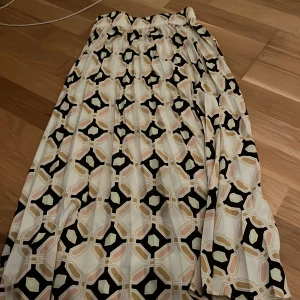 Mönstrad kjol med geometriskt mönster - Snygg kjol med geometriskt mönster i svart, beige och rosa. Kjolen har en elastisk midja för bekväm passform och är perfekt för en stilfull look.