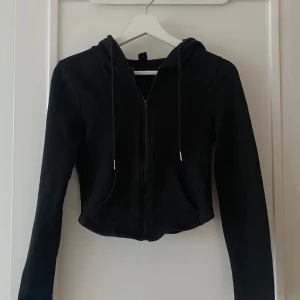 Svart croppad hoodie - Säljer en svart croppad hoodie med dragkedja och huva, knappt kommit till användning.
