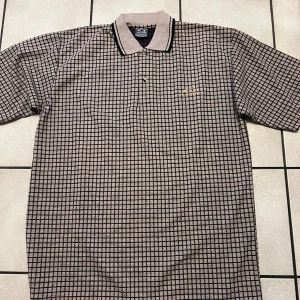 Rutig pikétröja från Software 100% bomull  - Snygg rutig pikétröja från Software i beige och svart. Tröjan har korta ärmar och en klassisk krage med knappar. Perfekt för en stilren look.