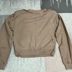 Beige sweatshirt - Säljer en beige sweatshirt med långa ärmar och ribbade muddar vid ärmslut och nederkant. Perfekt för en avslappnad stil.