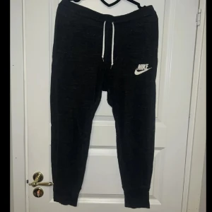 Svarta mjukisbyxor från Nike - Säljer ett par svarta mjukisbyxor från Nike med vit snörning i midjan och en vit Nike-logga på benet. Perfekta för en avslappnad stil. Nypris 500, använda 2-3 ggr