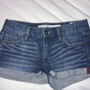 Blå jeansshorts från L.O.G.G. - Snygga blå jeansshorts från L.O.G.G. med klassisk femficksdesign och uppvikta benslut. Perfekta för en avslappnad stil. Märkeslapp i brunt läder baktill.