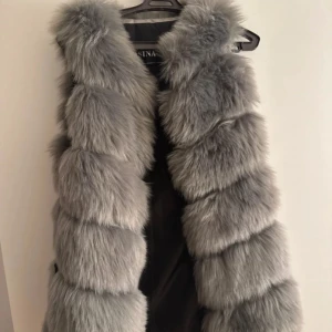 Grå pälsväst - Snygg och fluffig grå pälsväst som ger en lyxig känsla. Perfekt för att hålla sig varm och stilren under kyligare dagar. Västen har en mjuk och tät pälsstruktur som ger ett exklusivt utseende.