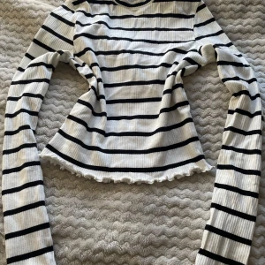 Randig ribbad tröja från H&M - Säljer en vit och svart randig ribbad tröja från H&M. Tröjan har långa ärmar och en vågig kant vid nederdelen som ger en fin detalj. Perfekt för en stilren look. Skriv gärna innan köp 😊