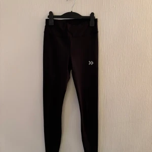 Svarta leggings med reflexdetalj - Snygga svarta leggings med en diskret reflexdetalj på benet. Perfekta för träning eller en aktiv vardag. De är tillverkade i ett stretchigt syntetmaterial som ger en tight passform och bra rörelsefrihet.