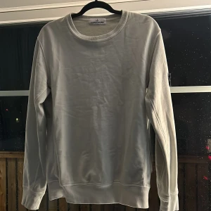 Vit sweatshirt från Stone Island - Säljer en stilren vit sweatshirt från Stone Island med rund hals och långa ärmar. Tröjan har en ikonisk logga på ärmen och ribbade muddar vid ärmslut och nederkant. Perfekt för en avslappnad look.