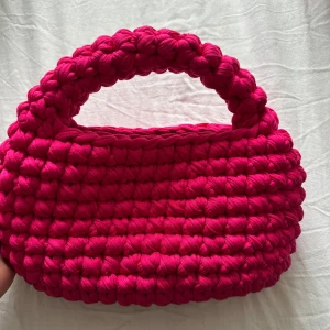 Rosa virkad handväska - Säljer en superfin rosa virkad handväska med ett unikt och chunky design. Perfekt för att ge din outfit en färgglad touch. Väskan har ett handtag som gör den lätt att bära med sig. Passar perfekt för dig som vill ha något annorlunda och trendigt.